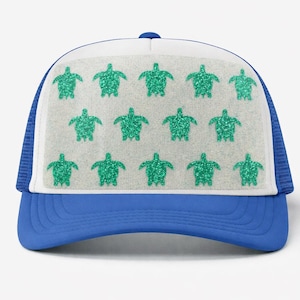 May include: A blue and white trucker hat with a blue brim and a white front panel. The front panel features a pattern of green glitter sea turtles. The hat has a mesh back.