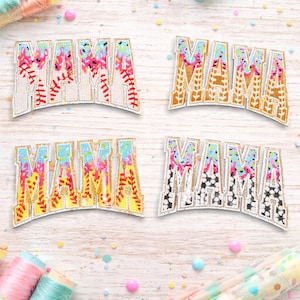 May include: Four decorative patches spelling "MAMA" in a variety of colorful designs. The patches feature glitter accents and are set against a light wood grain background. The letters are filled with floral, baseball, and geometric patterns.