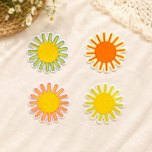 May include: Four circular embroidered patches shaped like suns with radiating rays. One patch is yellow with blue rays, one is orange with orange rays, one is yellow with pink rays, and one is yellow with light green rays, all featuring white borders.