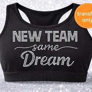 May include: Black sports bra with the text "NEW TEAM same Dream" in white rhinestones. The bra has a racerback design and a round orange sticker that says "transfer only".