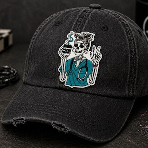 May include: Black distressed baseball cap with a patch featuring a skeleton in teal scrubs holding a coffee cup and making a peace sign. The cap has a curved brim and a distressed finish.