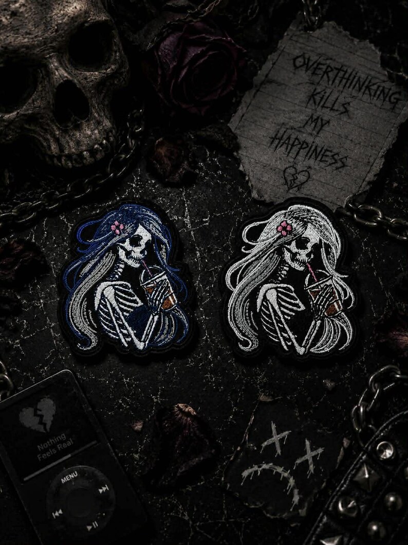 Pu&ograve; includere: Due toppe ricamate raffiguranti scheletri con capelli lunghi e bevande. Uno ha i capelli blu, l'altro bianchi. L'immagine include accessori gotici: un teschio, catene e un biglietto con la scritta "Overthinking Kills My Happiness". Il tema &egrave; dark e gotico.