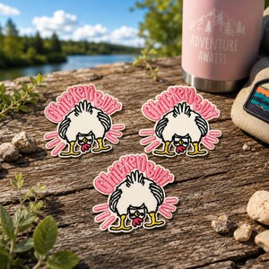 May include: Three embroidered patches featuring a white chicken bending over with its rear end facing upward. The text Chicken Butt is stitched in pink above the chicken. The design includes pink motion lines and yellow feet on a white background.