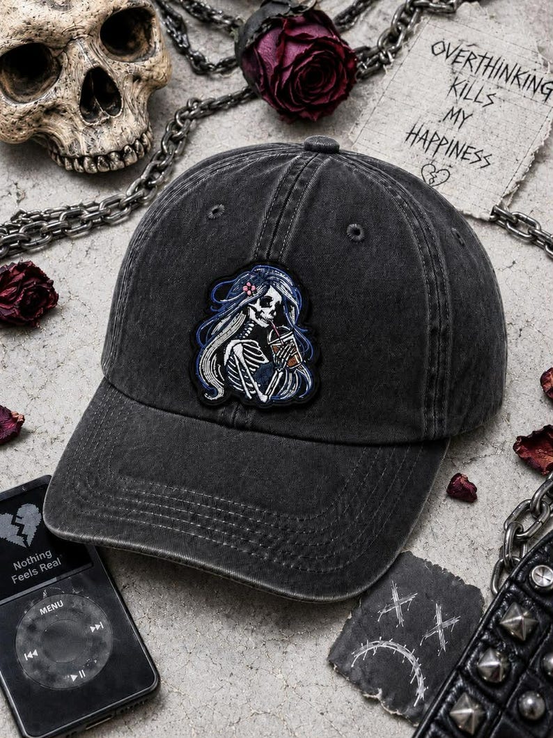 Pu&ograve; includere: Cappellino da baseball nero slavato con una toppa raffigurante uno scheletro con lunghi capelli blu che beve da una tazza. Il cappellino ha una visiera curva e un classico design a sei pannelli. Il testo "Overthinking Kills My Happiness" &egrave; visibile.