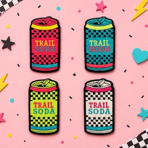 May include: Four embroidered patches shaped like soda cans, each featuring a checkered pattern and the text TRAIL SODA. The patches come in red, teal, lime green, and white colorways, all with black outlines and detailed pull-tab tops.
