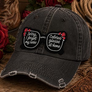 May include: A distressed black baseball cap with a patch featuring the text "Sorry I forgot my rose" and "Colored glasses at home". The patch is designed to look like eyeglasses with red rose accents. The cap has a pre-curved bill and distressed edges.