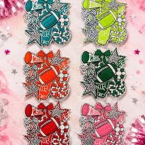 May include: Six embroidered patches featuring cheerleading and football motifs in teal, lime green, orange, dark green, red, and pink. Each patch includes a megaphone with the word CHEER, a football, a bow, a star, a flower, and a foam finger.