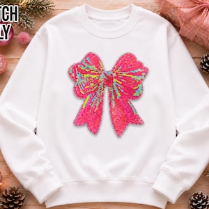May include: A white long-sleeve sweatshirt featuring a large, central bow graphic made of vibrant pink, yellow, and teal sequins. The text PATCH ONLY is printed in black in the upper left corner of the image, indicating the item is a decorative patch.
