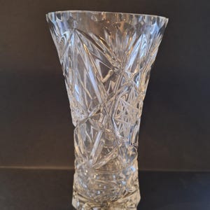 May include: Clear crystal vase with a geometric pattern. The vase has a wide, flared top and a faceted design that catches the light. The base is also faceted, adding to the overall decorative appeal. A classic piece for displaying flowers or as a decorative accent.