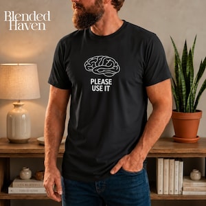 May include: A black short-sleeved t-shirt featuring a white line-art graphic of a human brain centered on the chest, positioned above the white text that reads "PLEASE USE IT" in a clean, sans-serif, capitalized font style.