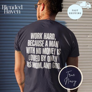 May include: A dark navy blue short-sleeved t-shirt featuring white text on the back that reads: WORK HARD, BECAUSE A MAN WITH NO MONEY IS LOVED BY ONLY HIS MOM, AND GOD. The shirt has a crew neckline and is made of a solid-colored fabric.