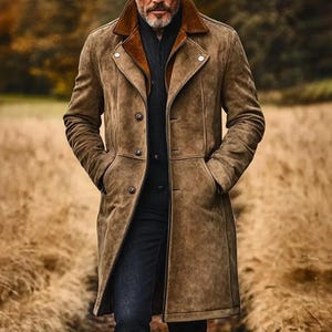 May include: A tan suede trench coat featuring a wide collar with a contrasting dark brown inner lining, a button-front closure, and two side pockets. The coat is worn over a black ribbed sweater and dark trousers, creating a layered appearance.