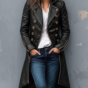 Peut inclure: Long manteau en cuir noir avec boutons et garnitures dorées. Le manteau est croisé et long. Le modèle porte un jean bleu et une chemise blanche. Un vêtement d'extérieur élégant.