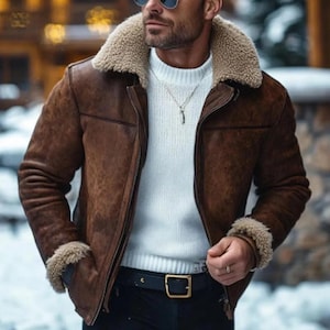 Puede incluir: Una chaqueta de ante marrón con cuello y puños de borreguillo beige, sobre un suéter de punto acanalado blanco. La chaqueta tiene cierre de cremallera frontal y el suéter se combina con un cinturón negro con hebilla rectangular dorada.