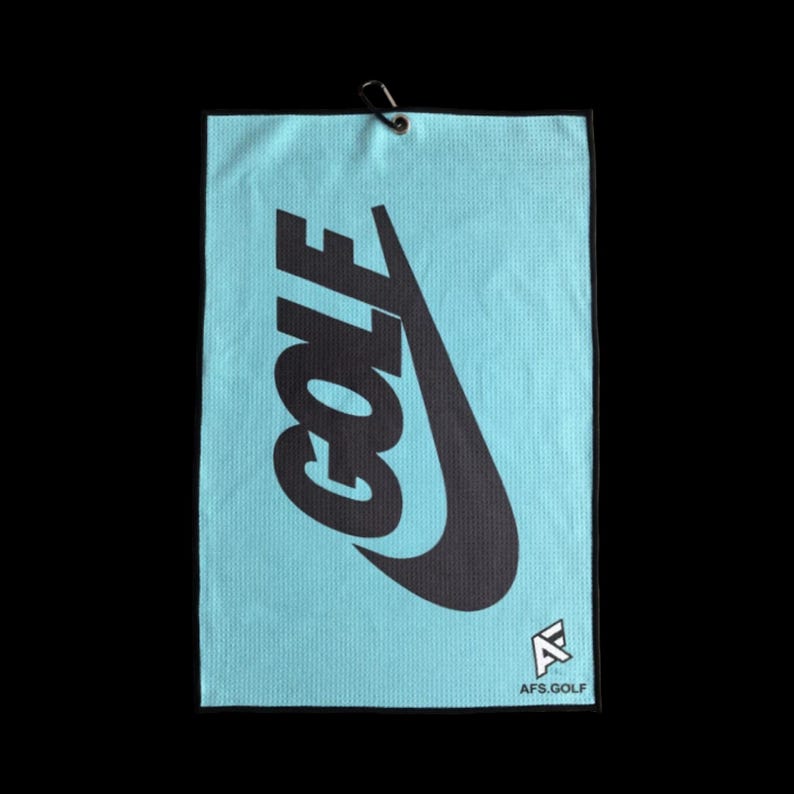 May include: A light blue golf towel with the word "GOLF" in large black letters, along with a black Nike swoosh. The towel has a black border and a small logo that says "AFS.GOLF". A black metal clip is attached to the top.