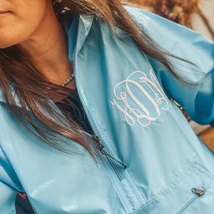 Puede incluir: Chaqueta anorak azul claro con cremallera de cuarto de cremallera y bolsillo delantero. La chaqueta presenta un monograma bordado blanco en el pecho. El anorak tiene capucha y tirador de cremallera. Fabricado con material ligero.