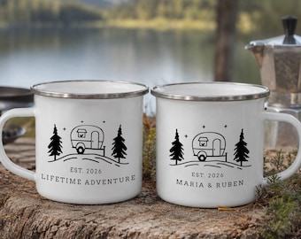 May include: Two white enamel mugs with silver rims, each featuring a black graphic of a camper trailer between two pine trees. One mug displays the text "EST. 2026" and "LIFETIME ADVENTURE," while the other shows "EST. 2026" and "MARIA & RUBEN."