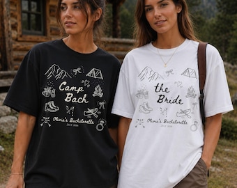 May include: A black t-shirt with white graphics and a white t-shirt with black graphics. Both feature illustrations of mountains, a tent, a campfire, boots, a canoe, and a ring, with the text Camp Bach or the Bride, Olivia's Bachelorette, July 2026.