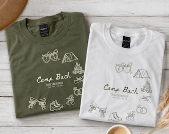 May include: An olive green t-shirt and a white t-shirt, each featuring a line art graphic with the text "Camp Bach", "Olivia's Bachelorette", and "Lake Tahoe - July 2024", alongside illustrations of hearts, a tent, campfire, rings, and boots.