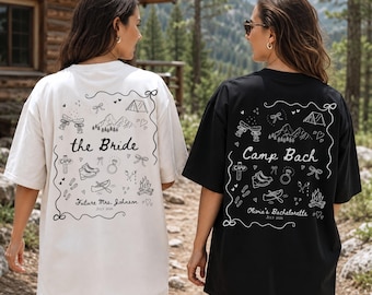 May include: A white t-shirt and a black t-shirt, each featuring a back graphic with line art of mountains, a tent, a campfire, a canoe, and a ring. The white shirt reads the Bride, Future Mrs. Johnson, July 2026. The black shirt reads Camp Bach, Olivia's Bachelorette, July 2026.