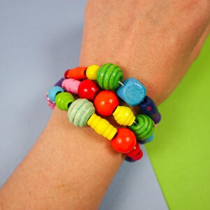 May include: A colorful wooden bead bracelet with a variety of shapes and sizes. The beads are painted in bright colors including red, yellow, green, blue, and pink. The bracelet is worn on a wrist.