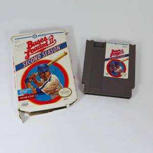 Könnte beinhalten: Eine Bases Loaded II Second Season Videospielkassette und die dazugehörige Pappschachtel. Die Schachtel zeigt einen Baseballspieler mit einem Schläger, das Jaleco-Logo und den Text No Booklet. Die graue Kassette hat ein passendes Etikett mit dem Titel.