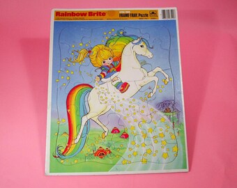 May include: A vintage Rainbow Brite frame-tray puzzle. The puzzle features a cartoon illustration of a girl riding a white unicorn with a rainbow tail. The puzzle has a blue background with yellow stars and the text "Rainbow Brite".