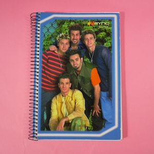 Puede incluir: Un cuaderno con espiral con un borde azul y una foto de la banda *NSYNC. La portada presenta a los miembros de la banda posando frente a un fondo verde. El texto "*NSYNC Journal" es visible en la esquina superior derecha.