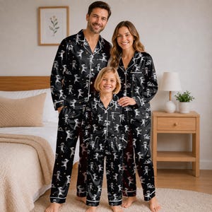 May include: Matching black pajama sets featuring a white mummy pattern and white piping. The long-sleeved button-down shirts have notched collars, and the long pants have an elastic waistband. The fabric is decorated with small yellow dots.