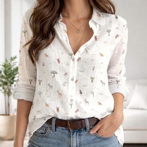 May include: A white long-sleeved button-down shirt featuring a repeating pattern of small, muted-colored safari animals and trees. The shirt has a classic collar, a front button placket, and sleeves that are rolled up at the cuffs.