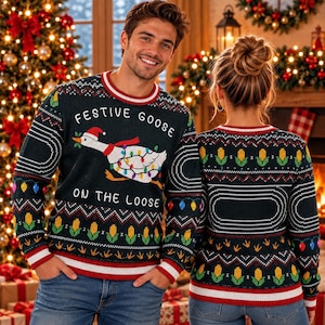 May include: A dark green long-sleeve knit sweater featuring a graphic of a goose wearing a Santa hat and wrapped in colorful Christmas lights. The text reads Festive Goose On The Loose. The sweater has a red and white striped crew neck and cuffs.