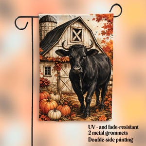 Puede incluir: Una bandera de jardín rectangular con un toro negro frente a un granero rústico con un silo. La escena incluye calabazas naranjas y blancas y hojas de otoño en el suelo. Texto: UV- and fade-resistant, 2 metal grommets, Double-side printing.