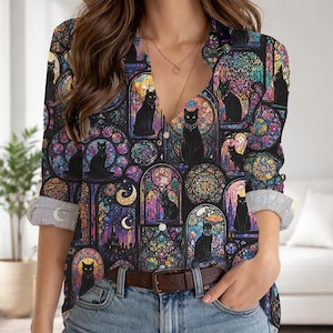 May include: A long-sleeved button-down shirt featuring a vibrant, multi-colored stained glass pattern. The design includes numerous black cat silhouettes set within arched window frames, accented by crescent moons and intricate geometric shapes.