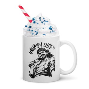 Può includere: Tazza in ceramica bianca con un'illustrazione in bianco e nero di uno chef che tiene un coltello, con la scritta "GRUMPY CHEF". La tazza è sormontata da panna montata, zuccherini blu e una cannuccia a righe rosse e bianche.