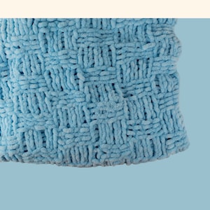 May include: A close-up of a light blue knitted baby blanket with a check pattern. The blanket is made with super chunky yarn and has a soft, fluffy texture. The text "Check Pattern Super Chunky Baby Blanket by Knitting Times Design" is visible at the top of the image.