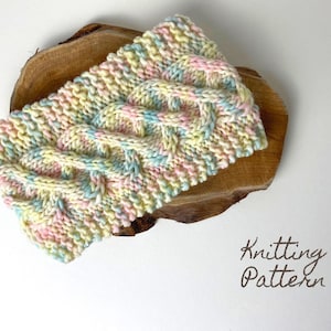 May include: A knitted headband in a pastel colour scheme with a cable knit pattern. The headband is displayed on a wooden surface.