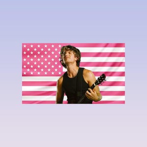 May include: A person playing a guitar against a pink American flag backdrop. The person is wearing a black vest top and has their eyes closed. The guitar is black.