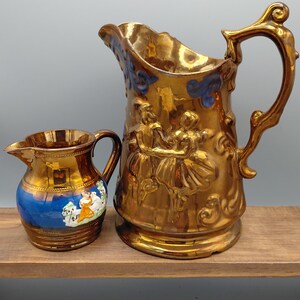 Juego de jarra y lechera de cobre antiguo con lustre, lote de cerámica figurativa victoriana, jarra con relieve de pareja bailando, par de piezas de loza con lustre de banda azul