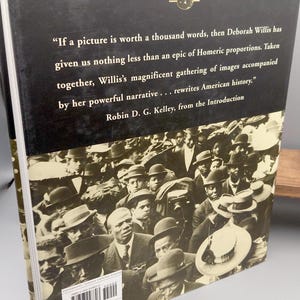 Puede incluir: Un libro de tapa dura titulado "REFLECTIONS IN BLACK" con una cubierta negra y una fotograf&iacute;a en tonos sepia de una multitud. El libro incluye una cita sobre el poder de las im&aacute;genes y la reescritura de la historia estadounidense.