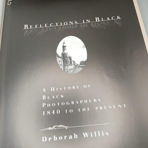 Puede incluir: Portada en blanco y negro del libro "Reflections in Black" de Deborah Willis. Presenta una imagen de un edificio y el texto "A History of Black Photographers 1840 to the Present".