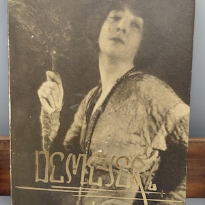 Może przedstawiać: Zdjęcie w stylu vintage w odcieniach sepii przedstawiające kobietę trzymającą wachlarz z piór. Obraz ma miękkie skupienie i klasyczną estetykę. Słowo "DCMESSE" jest wydrukowane na dole zdjęcia.