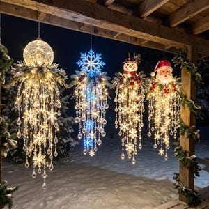 Op de afbeelding: Vier hangende kerstdecoraties met een gloeiende bol, een blauwe sneeuwvlok, een sneeuwpop en een kerstmanhoofd. Elk ornament heeft trapsgewijze strengen warmwitte LED-verlichting, heldere kristalachtige kralen en sneeuwvlokaccenten.