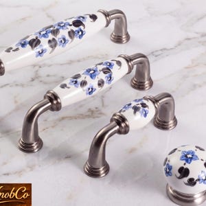 May include: Cabinet hardware set featuring three handles and a knob. The handles have a white porcelain center with blue floral designs and are paired with brushed nickel hardware. The knob has a matching floral design.