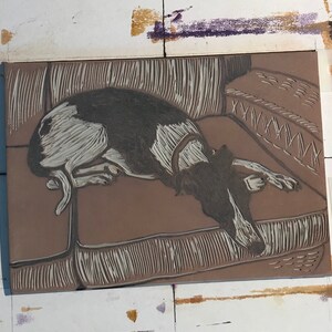 K&ouml;nnte beinhalten: Eine Nahaufnahme eines Linolschnitts, der einen schwarz-wei&szlig;en Hund zeigt, der auf einem Sofa liegt. Der Hund liegt entspannt mit dem Kopf auf dem Sofa. Der Druck ist detailliert und zeigt die Textur des Hundefells und des Sofas.