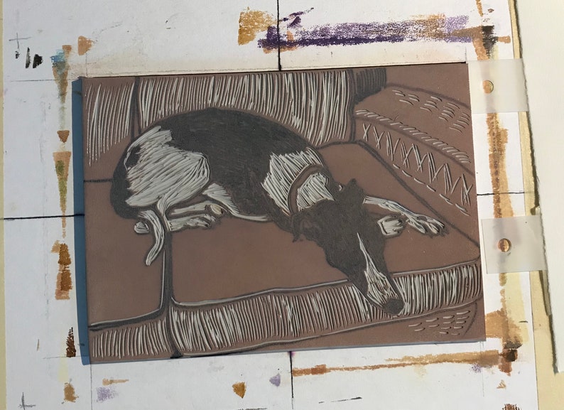 K&ouml;nnte beinhalten: Eine Nahaufnahme eines Linolschnitts, der einen schwarz-wei&szlig;en Hund zeigt, der auf einem Sofa liegt. Der Hund liegt entspannt mit dem Kopf auf dem Sofa. Der Druck ist detailliert und zeigt die Textur des Hundefells und des Sofas.
