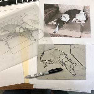 K&ouml;nnte beinhalten: Ein schwarz-wei&szlig;er Hund liegt auf einem gemusterten Kissen. Der Hund ist mit schwarzer Tinte auf einem wei&szlig;en Blatt Papier umrandet. Ein schwarzer Marker liegt auf einer grauen Oberfl&auml;che.