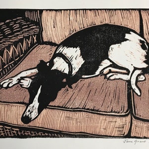 K&ouml;nnte beinhalten: Ein Schwarz-Wei&szlig;-Holzschnitt eines Hundes, der auf einem Sofa liegt. Der Hund blickt zur linken Seite des Bildes und hat seinen Kopf auf dem Sofa abgelegt. Das Sofa ist braun und hat ein gewebtes Muster. Der Druck ist unten rechts mit "Jane Grant Randall" signiert und unten links mit "2/10" nummeriert.