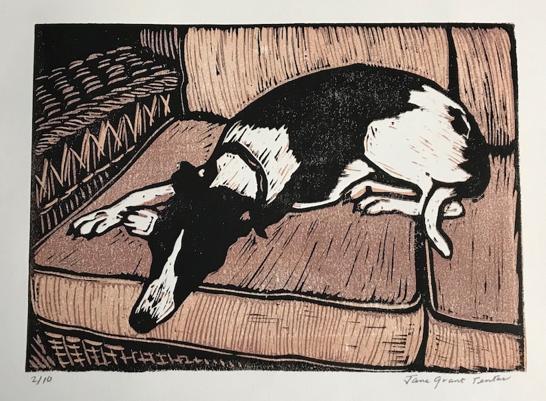 K&ouml;nnte beinhalten: Ein Schwarz-Wei&szlig;-Holzschnitt eines Hundes, der auf einem Sofa liegt. Der Hund blickt zur linken Seite des Bildes und hat seinen Kopf auf dem Sofa abgelegt. Das Sofa ist braun und hat ein gewebtes Muster. Der Druck ist unten rechts mit "Jane Grant Randall" signiert und unten links mit "2/10" nummeriert.