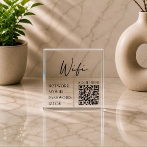 May include: A clear acrylic square sign featuring black printed text and a QR code. The text reads Wifi, Network: MYWIFI, Password: 123456, and Scan Here. The sign is designed for displaying wireless internet credentials in a home or business setting.