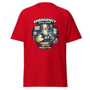 Puede incluir: Camiseta roja con un pato de dibujos animados con auriculares y chaleco, con el texto "Emergency Duck Crew" y "Always on Call". El diseño incluye gráficos de servicios de emergencia como un teléfono, un mapa y pantallas de ordenador.